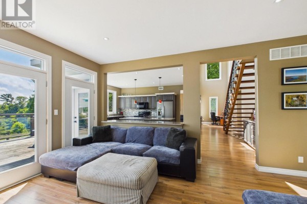 Open concept living area with sectional sofa, view of kitchen and wood staircase. - 180 Allison's Point Road, Huntsville