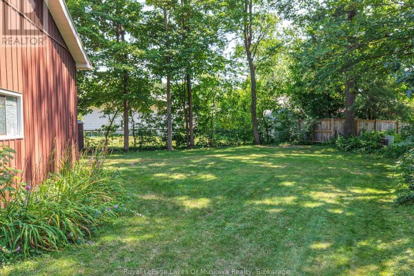 Backyard view of a green lawn surrounded by trees and a wooden fence. - 180 Lofty Pines Crescent, Gravenhurst)