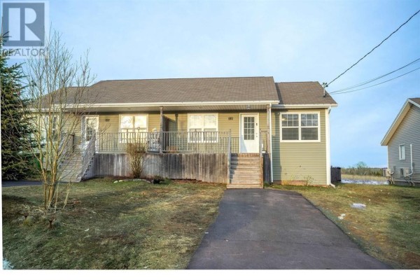 View of the exterior from the left, showing a light green townhouse with a front deck and steps. - 180 Norwood Road, Charlottetown