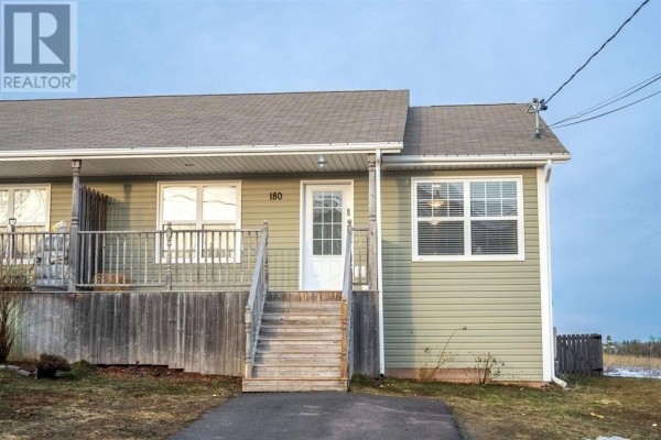 Detail of the right side of the townhouse exterior, showing light green siding, windows, and HVAC units. - 180 Norwood Road, Charlottetown