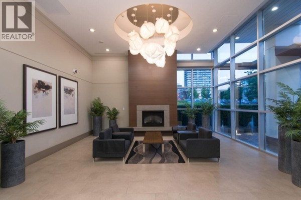 Building lobby with a fireplace, modern seating, large windows, and decorative lighting fixture. - 1801 158 W 13th Street, North Vancouver