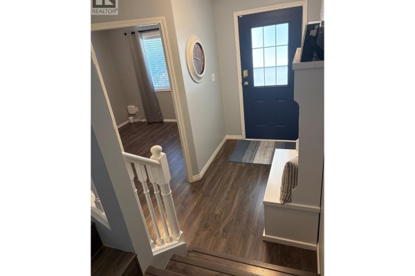 Entrance hall with dark blue front door, grey walls, dark wood flooring, and a white bench. - 1801 53 Avenue Unit# 111, Vernon