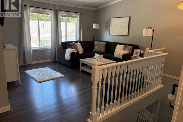 Living room with a dark sectional couch, white coffee table, and large windows with grey curtains. - 1801 53 Avenue Unit# 111, Vernon