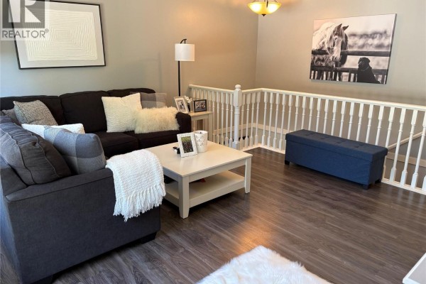 Living room with a dark sectional couch, white coffee table, and white railing overlooking stairs. - 1801 53 Avenue Unit# 111, Vernon