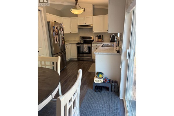 Kitchen with white cabinets, stainless steel appliances, granite countertops, and a dining table with chairs. - 1801 53 Avenue Unit# 111, Vernon
