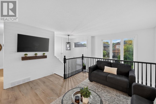 Living area with a mounted TV, black railings, and two sofas with windows overlooking the neighborhood. - 1801 Seymour Crescent, London North