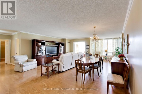 Living and dining room with light wood floors, white sofa, dark wood media unit, and oval dining table. - 1802 - 1 Clark Avenue W, Vaughan