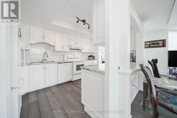 Renovated kitchen with white cabinets, granite counters, and wood floors - 1802 - 8 Lisa Street Brampton