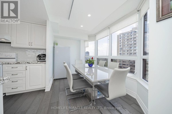 Dining area with white table, modern chairs, and kitchen view. - 1802 - 8 Lisa Street, Brampton