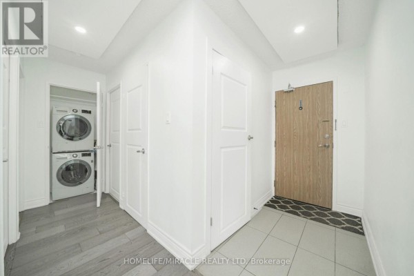 Stacked washer and dryer, wood-look flooring, and tile flooring in hallway - 1802 - 8 Lisa Street Brampton
