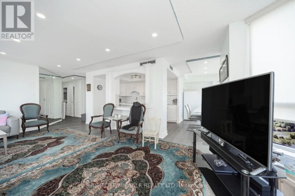 Living room with ornate chairs, large rug, and TV, opening to kitchen - 1802 - 8 Lisa Street Brampton