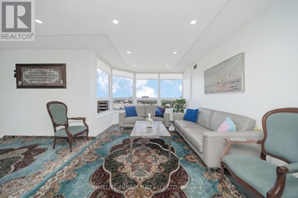 Living room with bay windows, sofas, coffee table, ornate rug. - 1802 - 8 Lisa Street Brampton