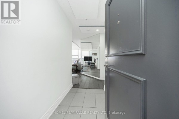 Hallway with gray door leading to living area with mirrored wall and sofa - 1802 - 8 Lisa Street Brampton