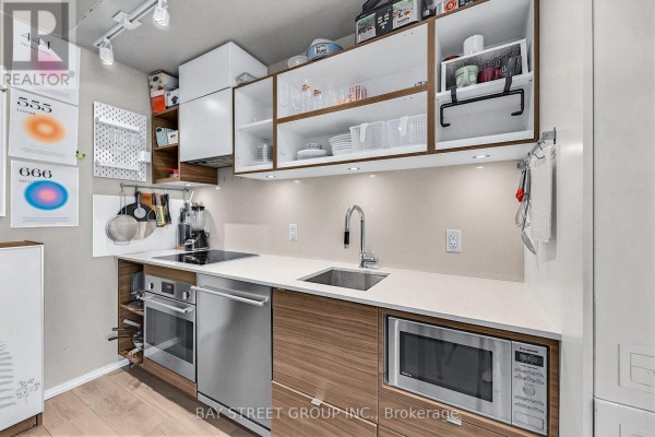 Close-up of apartment kitchen with induction cooktop, oven, dishwasher, microwave, and stainless steel sink. - 1803 - 125 Peter Street, Toronto