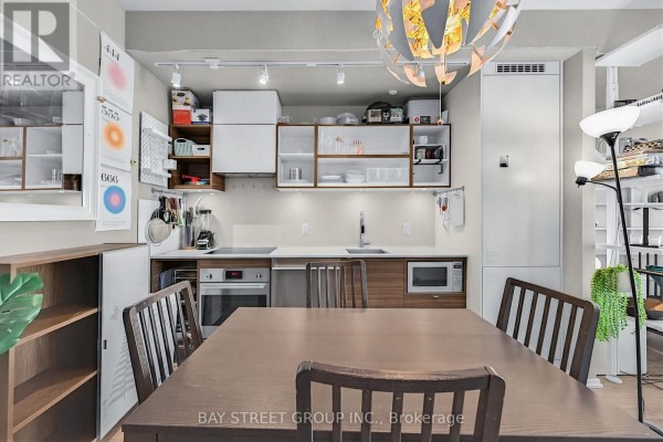 Apartment dining table with wooden chairs, overlooking the kitchen with white and wood cabinetry. - 1803 - 125 Peter Street, Toronto