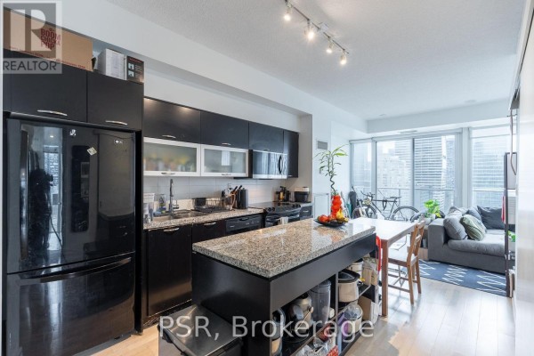 View of an open-concept living space featuring a modern kitchen with black cabinets and a granite island. - 1803 - 126 Simcoe Street, Toronto
