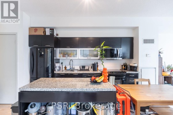 Kitchen island with granite countertop, black base, and storage, adjacent to a dining table and black kitchen cabinets. - 1803 - 126 Simcoe Street, Toronto