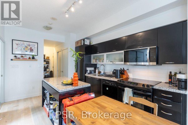 A contemporary kitchen with dark wood cabinets, granite countertops, and an island, connected to a hallway. - 1803 - 126 Simcoe Street, Toronto
