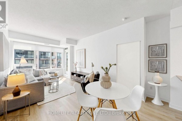 Dining area with white chairs and table, adjacent to the living room with large windows. - 1804 - 55 East Liberty Street, Toronto