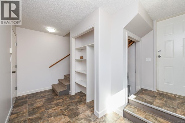 An interior hallway with tiled flooring, a staircase, and white-painted doors and storage shelving. - 1804 Little River Rd, Comox