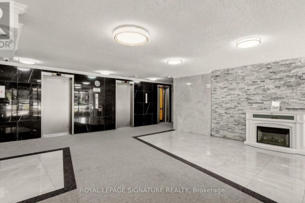 Interior view of the apartment building lobby with elevators, marble walls, and a decorative fireplace. - 1805 - 4 Kings Cross Road, Brampton