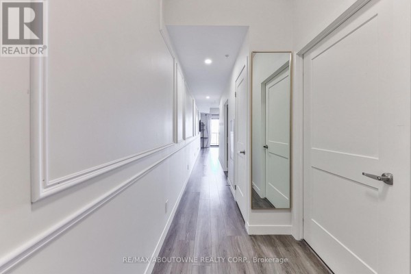Long hallway leading to the apartment with light-colored walls and a mirror, showcasing laminate flooring. - 1806 - 15 Queen Street, Hamilton