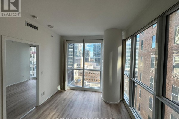 Living room with city views, light wood floors, and a curved column. - 1806 - 70 Temperance Street, Toronto