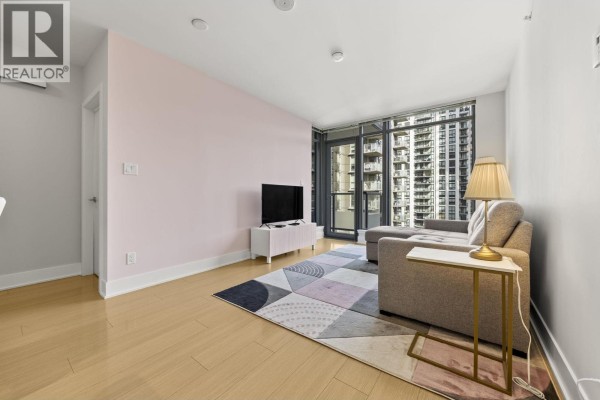Living room with light wood floors, pink accent wall, and view of city buildings from balcony. - 1806 1188 Pinetree Way, Coquitlam
