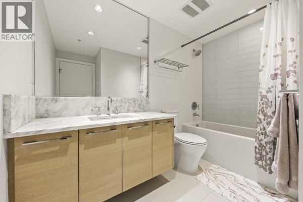 Bathroom with marble countertop vanity, wooden cabinets, and white tile shower/tub. - 1806 1188 Pinetree Way, Coquitlam