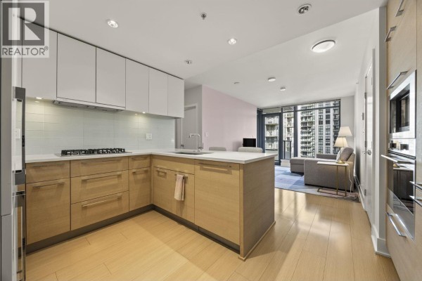 Modern L-shaped kitchen with light wood cabinets and white countertops connected to living area. - 1806 1188 Pinetree Way, Coquitlam