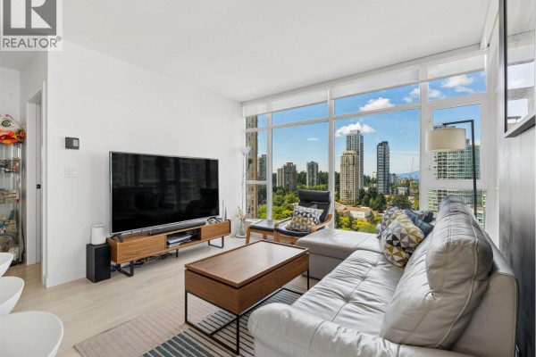 Living room with a sectional sofa, large TV, coffee table, and floor-to-ceiling windows. - 1807 6098 Station Street, Burnaby