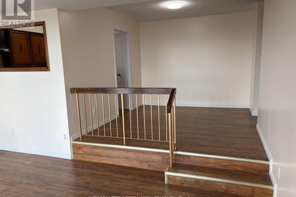 Interior view of a living area with wood-look flooring and a railing leading to a step. - 1808 - 1338 York Mills Boulevard, Toronto