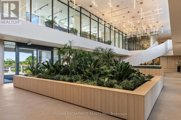 Modern lobby with a large planter of greenery, light-colored tile floors, and a staircase with a textured wall. - 1808 - 3079 Trafalgar Road, Oakville