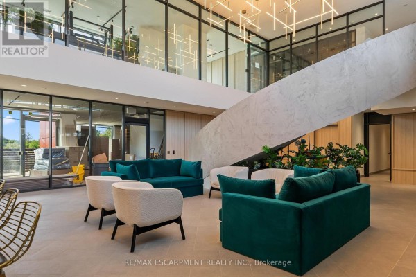 Contemporary lobby seating area with teal sofas and white armchairs in front of a large staircase and floor-to-ceiling windows. - 1808 - 3079 Trafalgar Road, Oakville