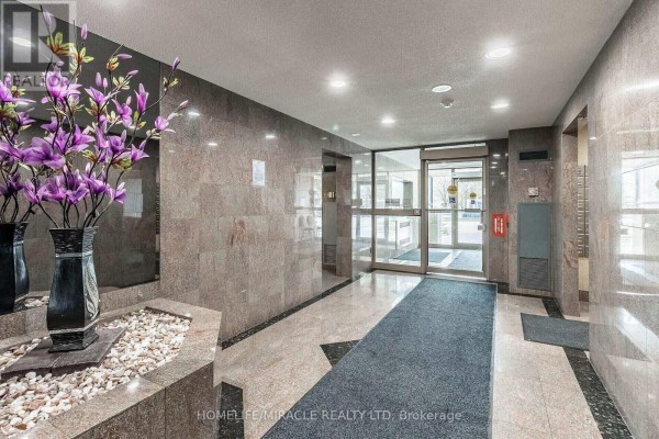 Building lobby with marble-patterned walls, blue carpet runner, and decorative flowers. - 1809 - 30 Malta Avenue, Brampton