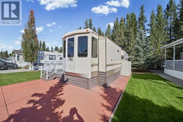 Side view of mobile home with a red concrete driveway and green grass. - 181, 32379 Range Road 55, Rural Mountain View County