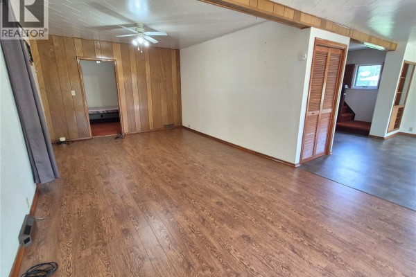 Interior view of a living room with wood-look laminate flooring and wood-paneled walls, leading to a staircase. - 181 2nd Street W, Bengough
