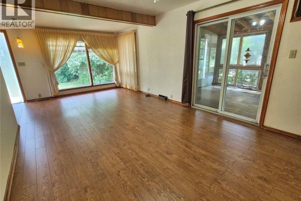 Interior view of a living area with wood-look laminate flooring, a large picture window, and a sliding glass door to a screened-in porch. - 181 2nd Street W, Bengough