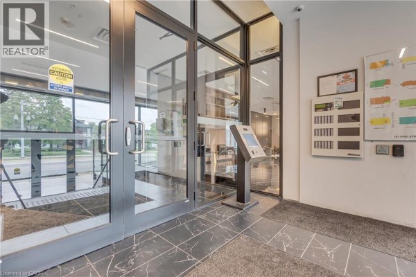Entrance to the building lobby with glass doors, an information kiosk, and a security camera. - 181 King Street S Unit# 1408, Waterloo