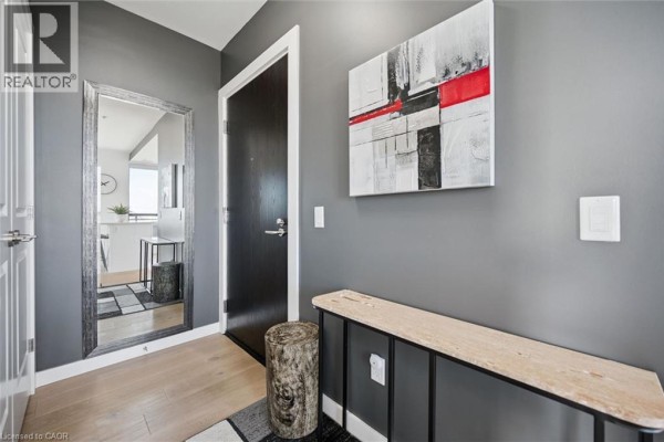 Apartment entryway with grey walls, a dark wood door, and a full-length mirror. - 181 King Street S Unit# 1714, Waterloo