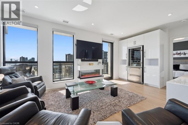 Living room with leather chairs, a glass coffee table, and a modern fireplace. - 181 King Street S Unit# 1714, Waterloo
