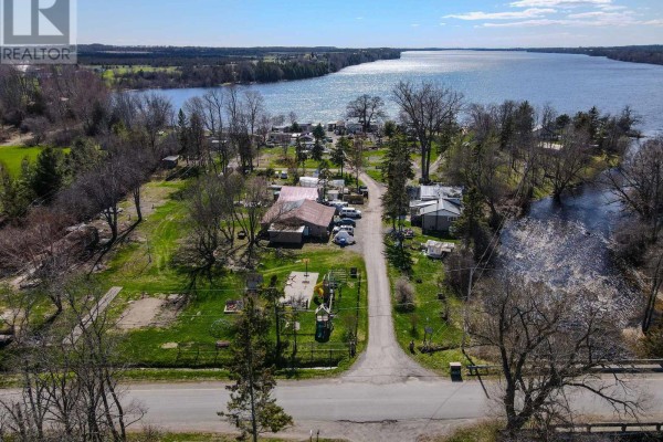 Waterfront view of mobile homes and small cabins situated along a dark body of water. - 181 Melville Road, Prince Edward County