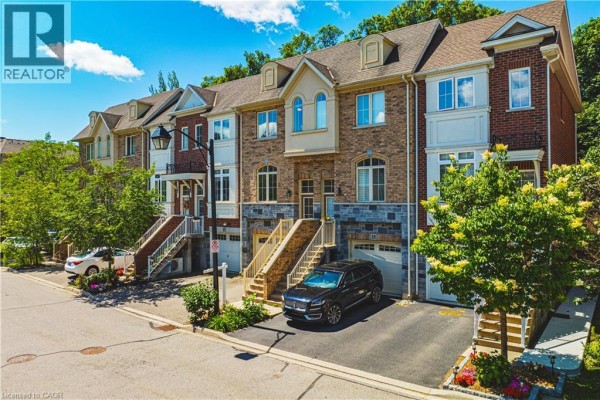 Front exterior of townhouse unit 14 featuring beige brick, stone, and a dark SUV. - 181 Plains Road W Unit# 14, Burlington