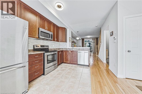 Kitchen with wood cabinets, stainless steel appliances, tiled backsplash, and wood flooring. - 181 Plains Road W Unit# 14, Burlington