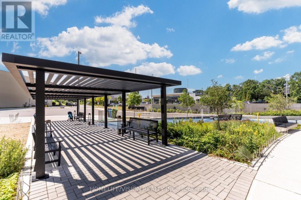 Outdoor covered seating area with black benches and a paved walkway next to a water feature. - 1810 - 30 Inn On The Park Drive, Toronto