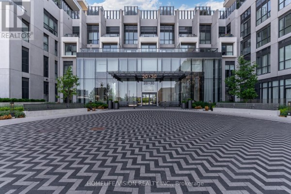 Entrance to a modern apartment building with a glass facade and a patterned driveway. - 1810 - 30 Inn On The Park Drive, Toronto