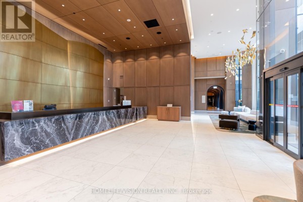 Building lobby featuring a marble reception desk, wood paneling, and a modern chandelier. - 1810 - 30 Inn On The Park Drive, Toronto