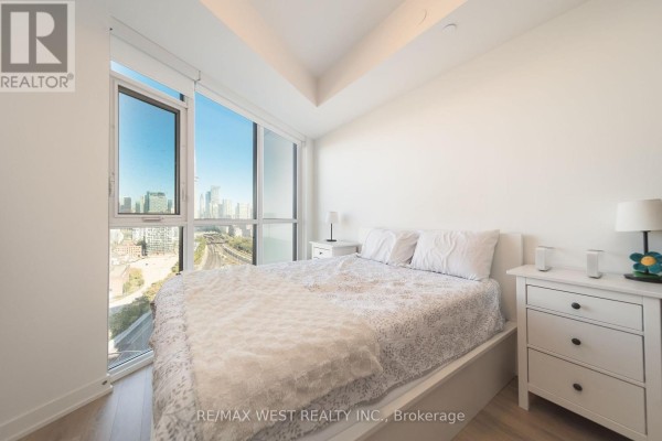 Bedroom with queen bed, nightstands, and large window overlooking the city. - 1810 - 50 Ordnance Street, Toronto