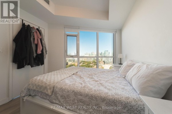 Bedroom with a large window, bed, and open closet with hanging clothes. - 1810 - 50 Ordnance Street, Toronto
