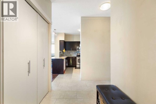 Hallway leading to an open-concept kitchen area with dark wood cabinets. - 1811, 8710 Horton Road Sw, Calgary